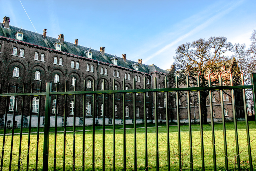 Fachada lateral de la Abadía de Keizersberg con césped y valla metálica, Leuven, Bélgica.