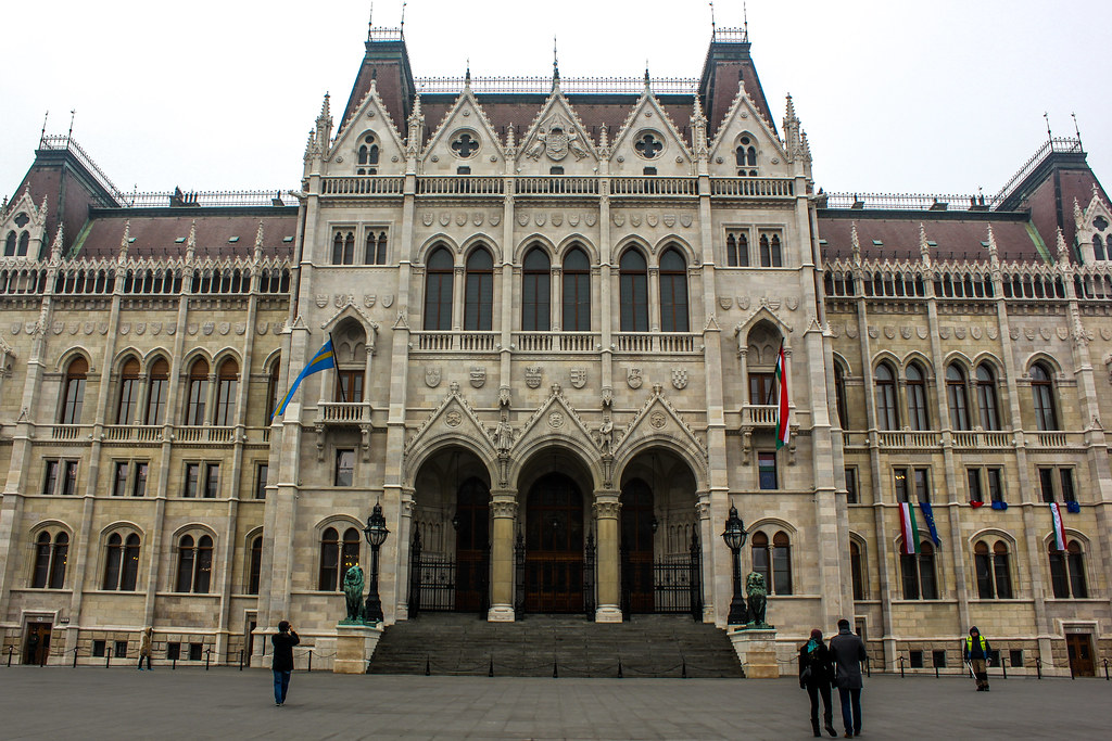 Antigua entrada principal del Parlamento de Budapest con banderas y estatuas.
