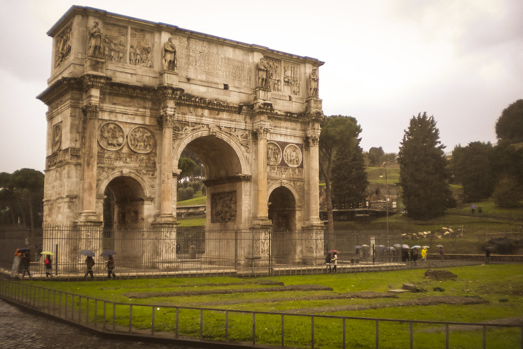 Arco de Constantino en Roma en un día nublado con turistas paseando cerca.