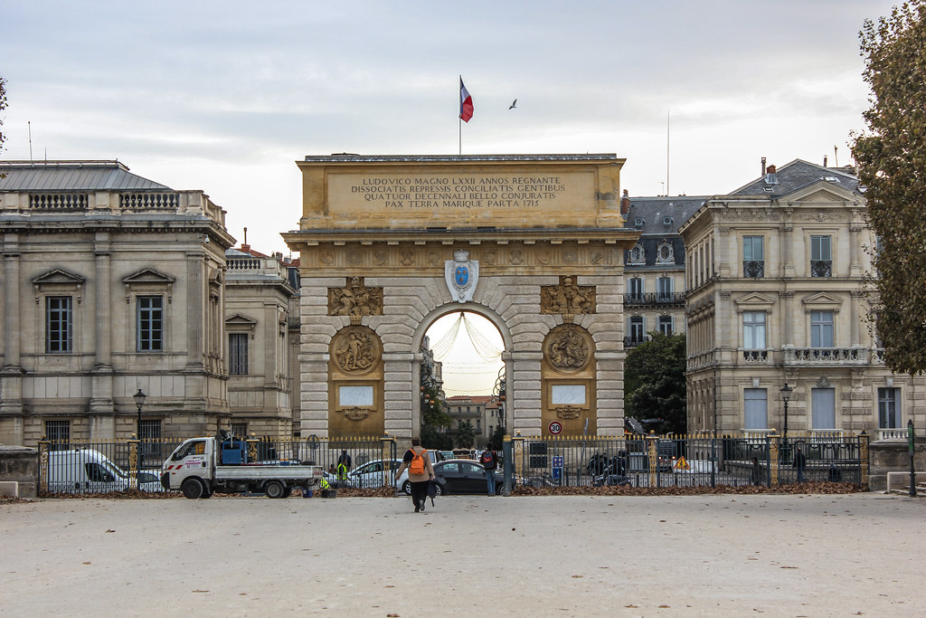 Arco del Triunfo en la Plaza Real del Peyrou en Montpellier, con peatones y edificios históricos.