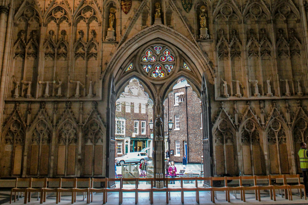 Vista interior del arco gótico de la Catedral de York Minster con vitrales y edificios exteriores al fondo.