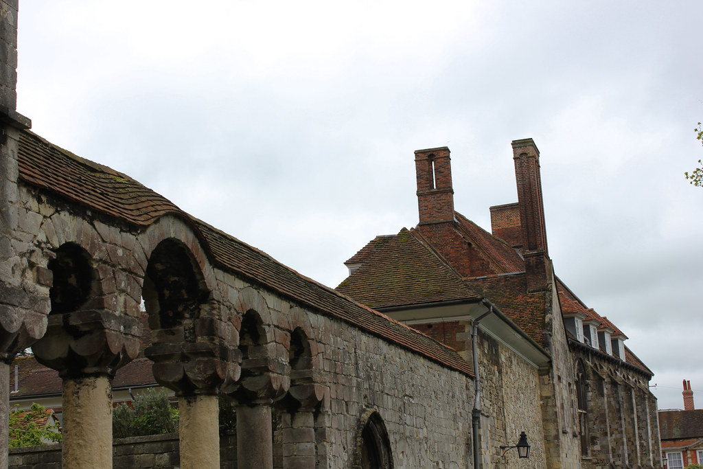 Arcos medievales de piedra en Winchester con casa tradicional al fondo.