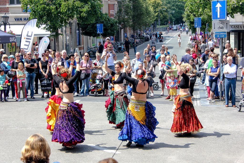 Bailarinas de danza del vientre actuando en una calle con espectadores disfrutando del evento al aire libre.