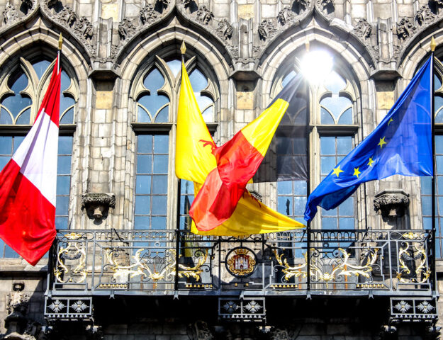 Banderas de Mons, Valonia, Bélgica y la Unión Europea ondeando en la fachada del Ayuntamiento de Mons, Bélgica.