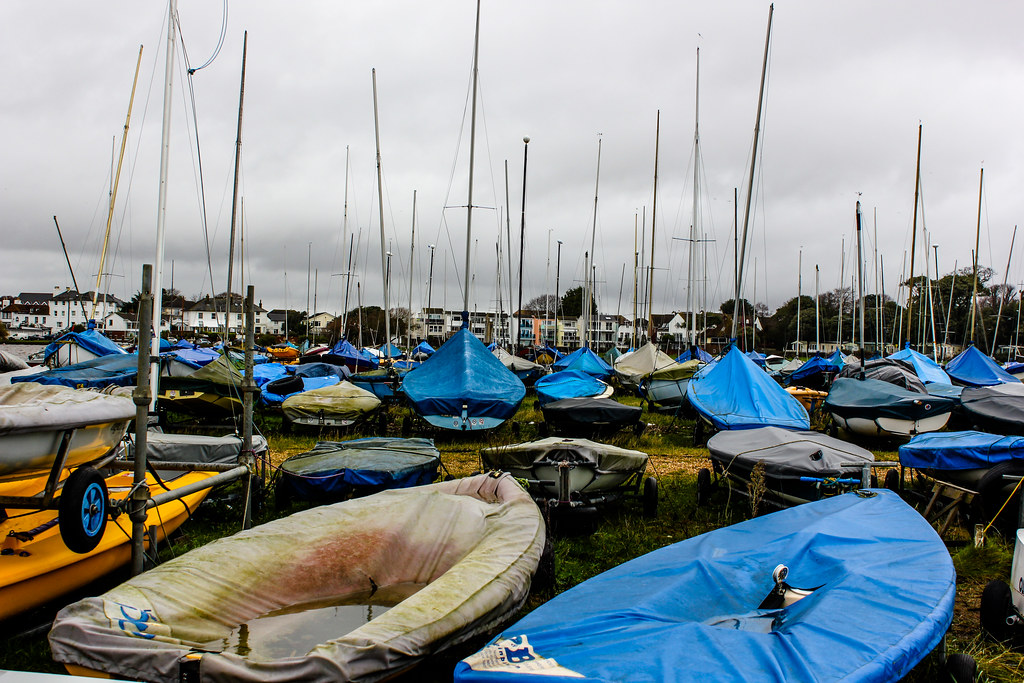 Barcos de vela almacenados con fundas en Mudeford Quay en un día nublado.