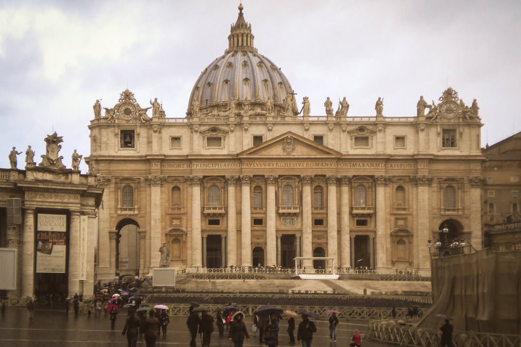 Fachada de la Basílica de San Pedro en el Vaticano en un día lluvioso con visitantes con paraguas.