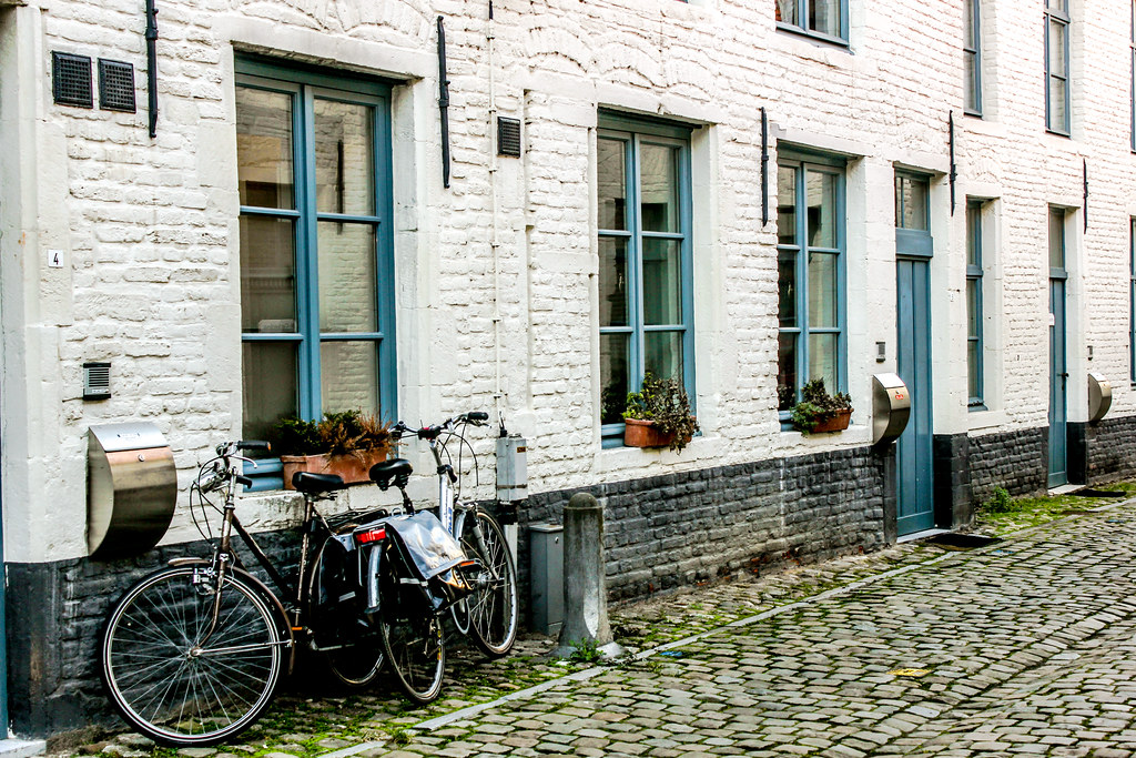 Bicicletas aparcadas en la calle adoquinada del Klein Begijnhof con casas blancas en Lovaina.