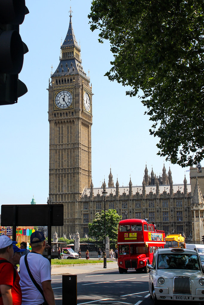 Big Ben y el Palacio de Westminster en Londres, con un autobús turístico rojo y un taxi tradicional en primer plano.