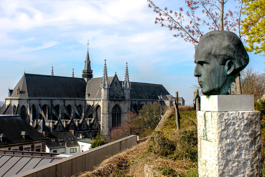 Escultura de busto en primer plano con la Colegiata de Santa Waudru al fondo en Mons, Bélgica.