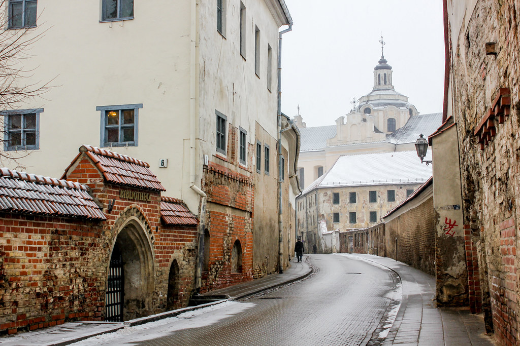 Calle empedrada con edificios antiguos y la cúpula de una iglesia en el fondo en Vilna, Lituania, en invierno.