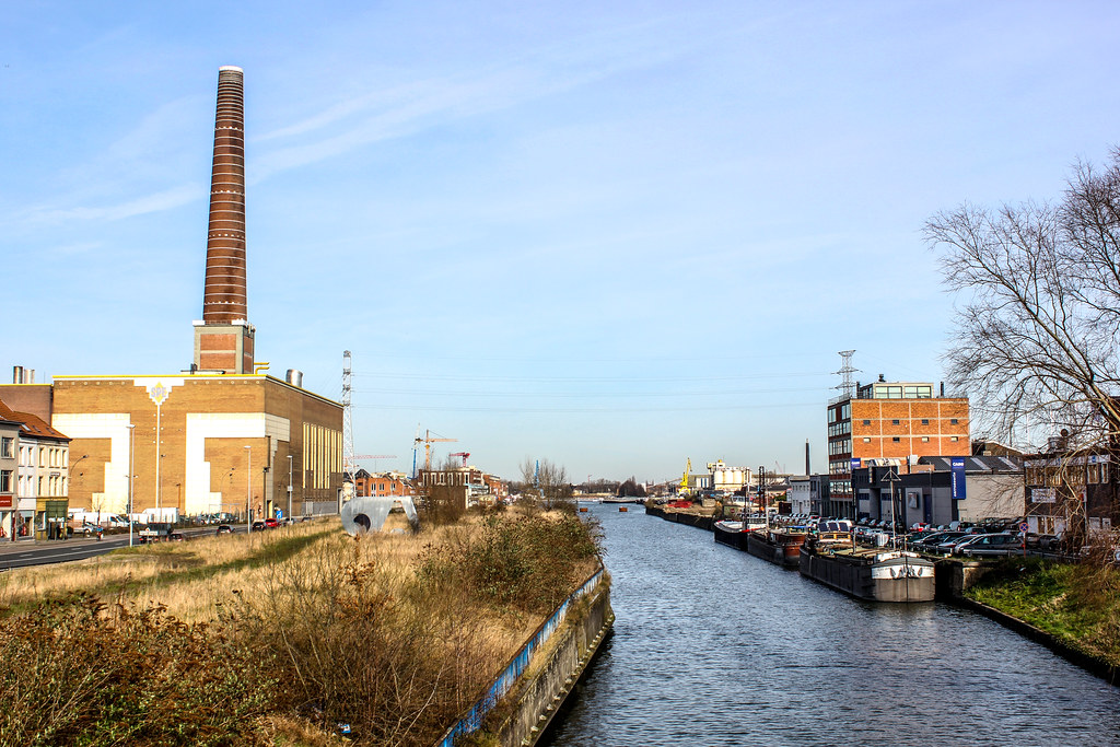 Canal de Gante con chimenea industrial y embarcaderos en un día soleado.