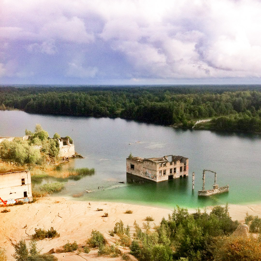 Cantera de Rummu sumergida en Estonia con estructuras abandonadas y bosque circundante bajo cielo nublado.