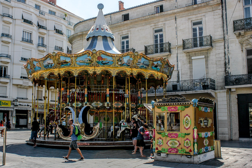 Carrusel tradicional en la Place de la Comédie de Montpellier con peatones y edificios históricos.