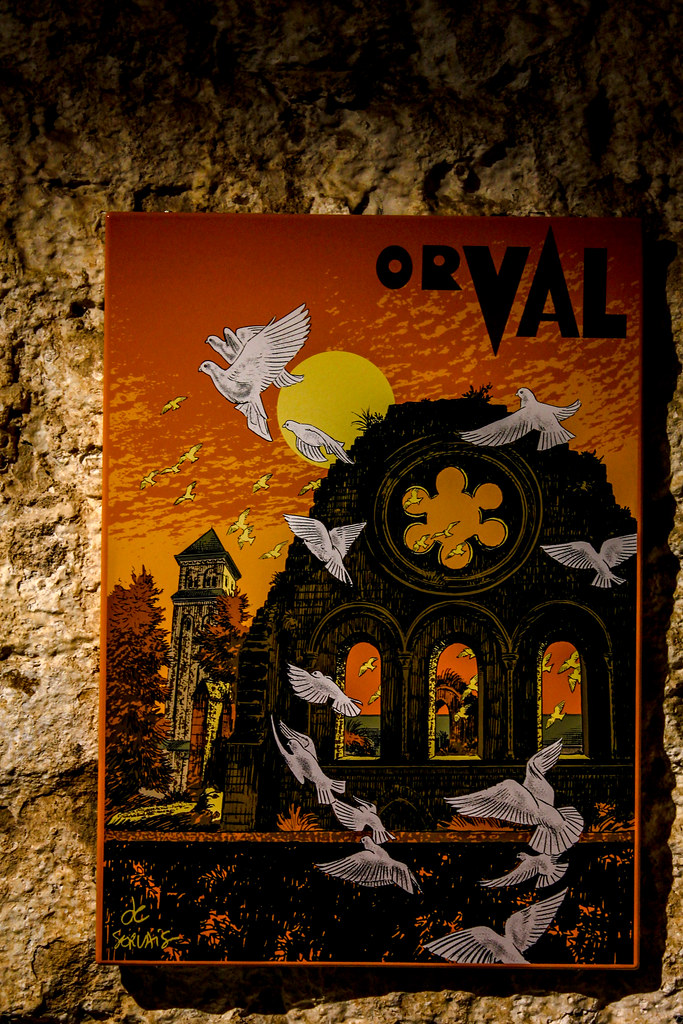 Cartel artístico de cerveza Orval con palomas volando y la abadía de fondo.
