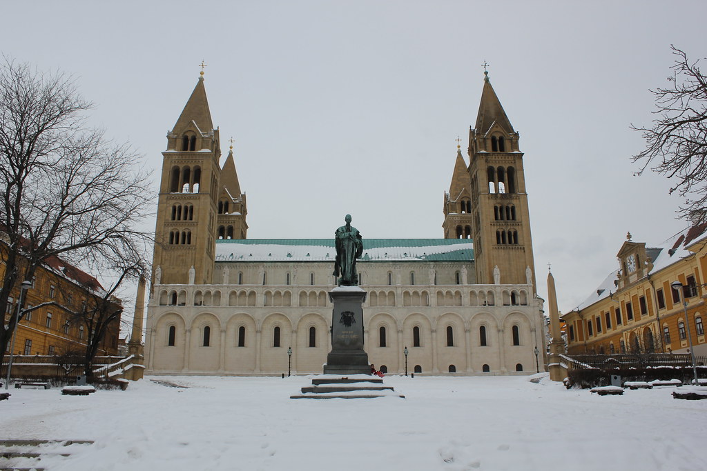 Catedral de Pécs cubierta de nieve con estatua en primer plano.