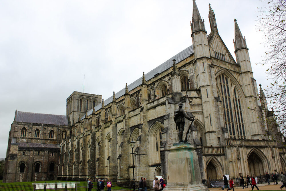 Catedral de Winchester con estatua de soldado en primer plano y visitantes alrededor.