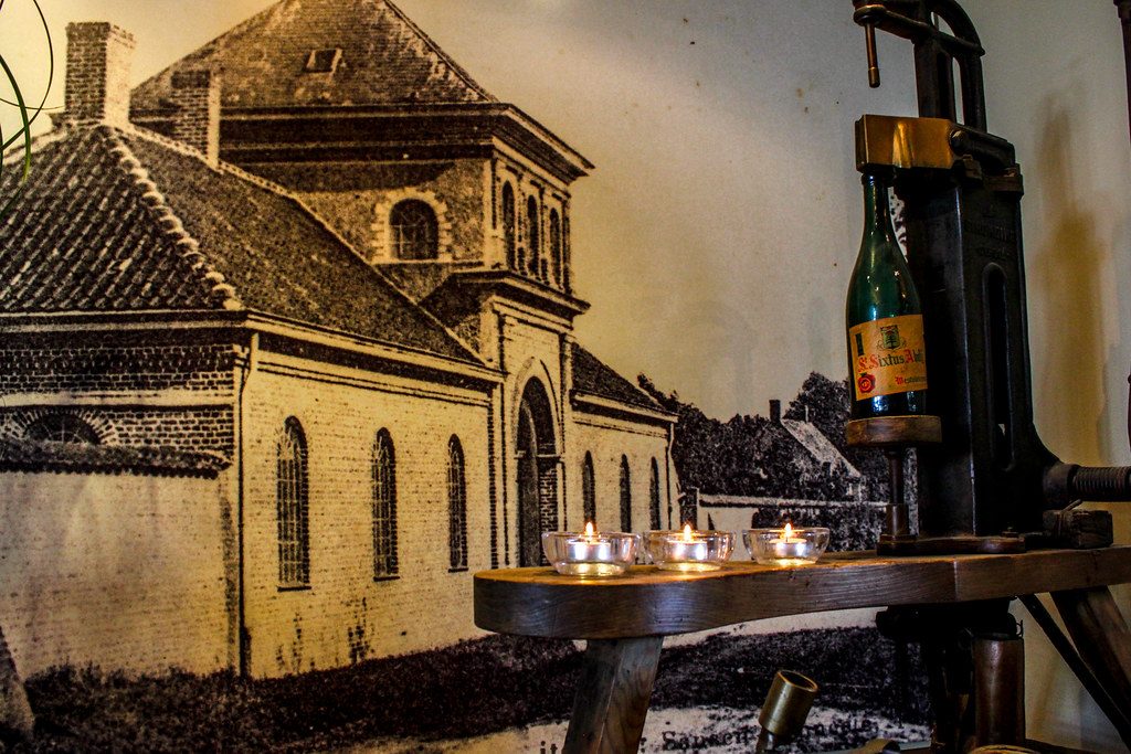 Cerveza en una prensa antigua con velas y una imagen de la Abadía de Westvleteren en el fondo.