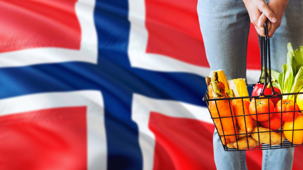 Cesta de compras con verduras frescas y la bandera de Noruega de fondo.