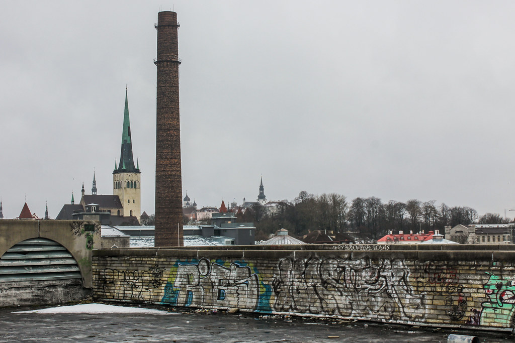 Chimenea industrial con grafitis en primer plano y la iglesia de San Olaf al fondo en Tallin.