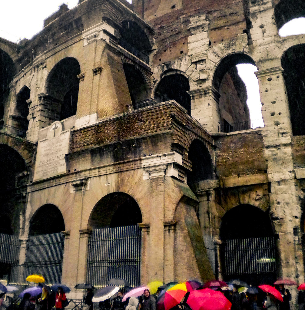Cola en la entrada del Coliseo de gente con paraguas.