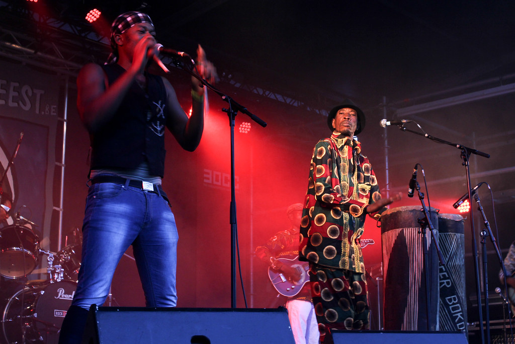 Cantante africano y percusionista actuando en vivo en un festival con iluminación roja de fondo y set de batería Pearl.