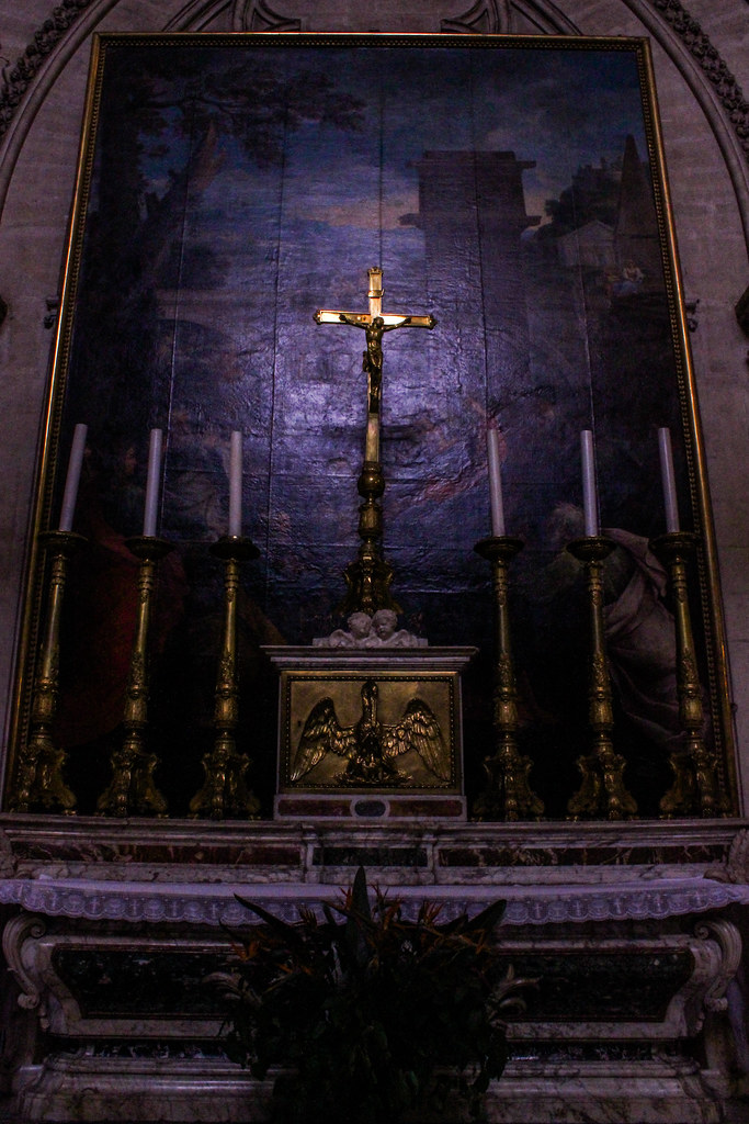 Crucifijo sobre un altar con detalles dorados en un fondo de tapiz azul en la catedral de Montpellier.