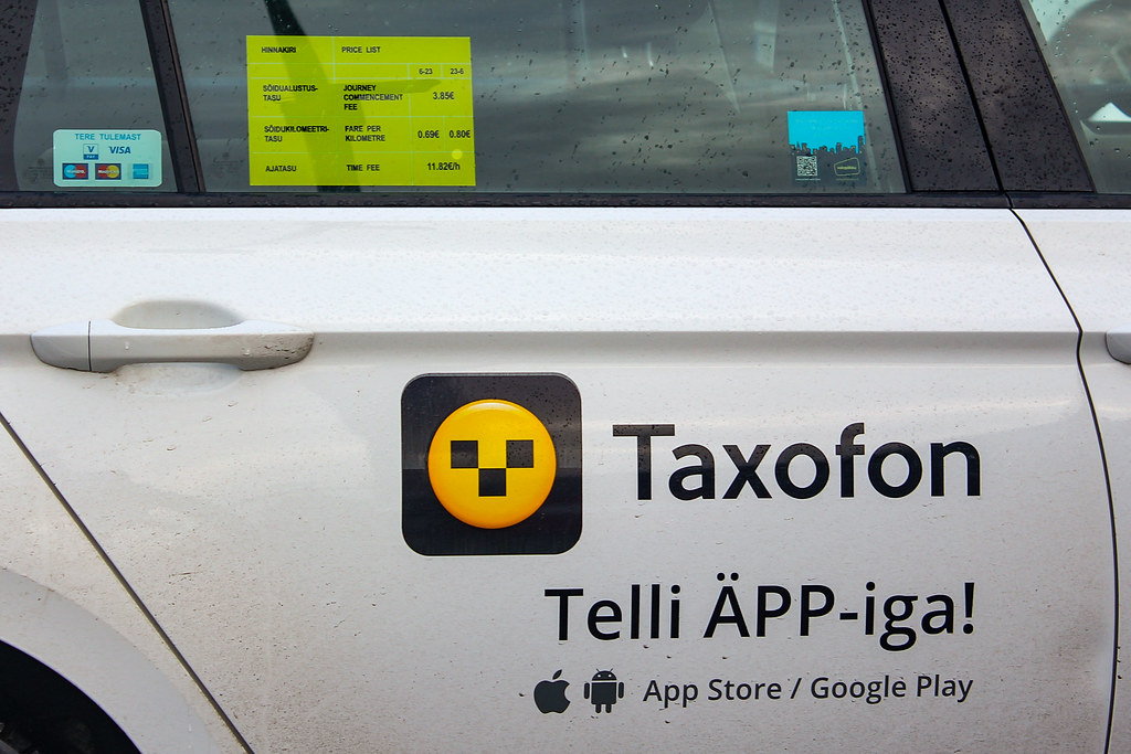 Detalle de un taxi con publicidad de Taxofon y lista de precios en la ventana en Tallin.