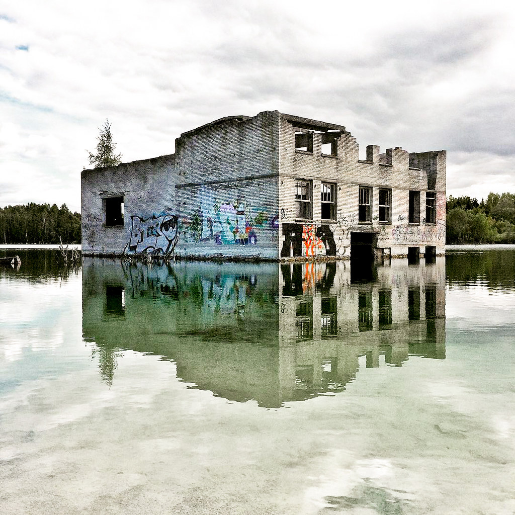 Edificio abandonado con grafitis reflejado en el agua tranquila de la cantera de Rummu, Estonia.