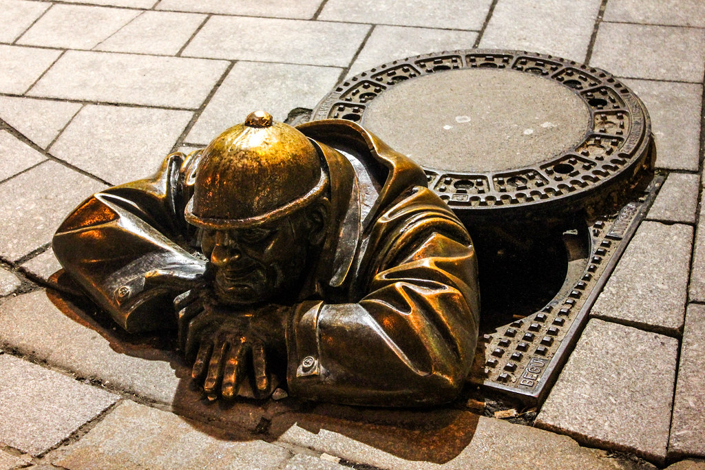 Escultura de bronce de Čumil, el trabajador de alcantarillado, asomándose desde una tapa de alcantarilla en las calles adoquinadas de Bratislava