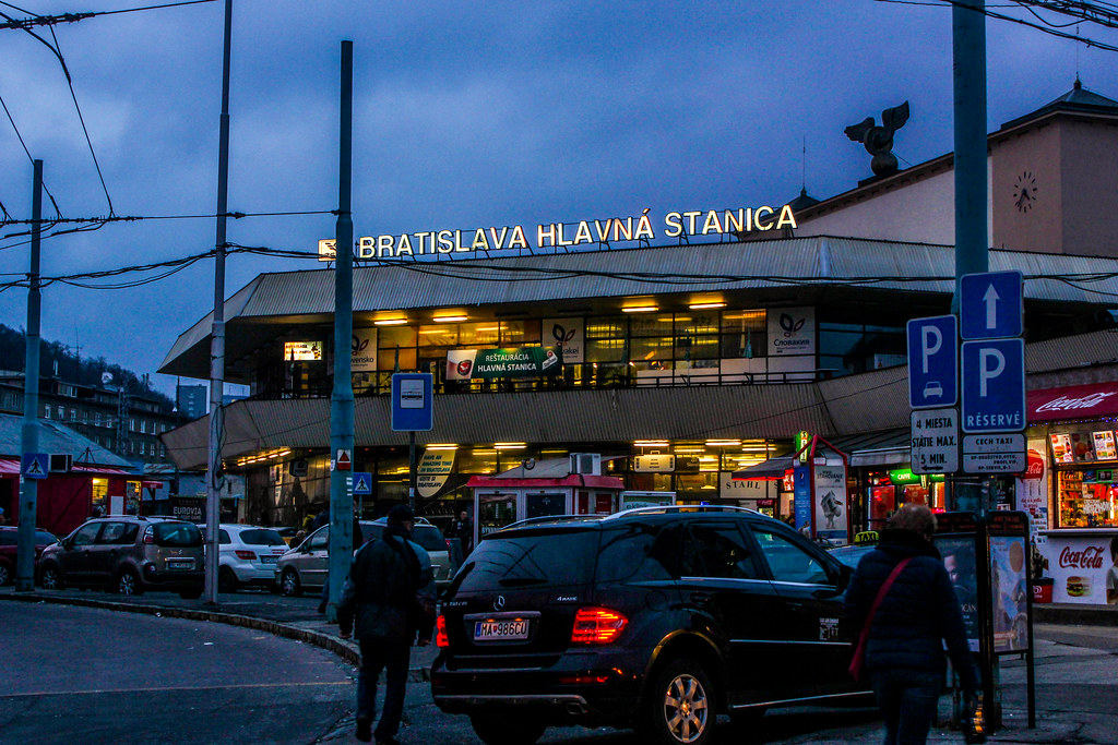 Estación de tren principal de Bratislava (Bratislava Hlavná Stanica) al atardecer con transeúntes y vehículos.