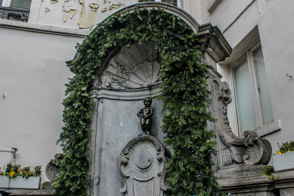 Estatua del Manneken Pis de Bruselas rodeada de hiedra verde en su icónica fuente.