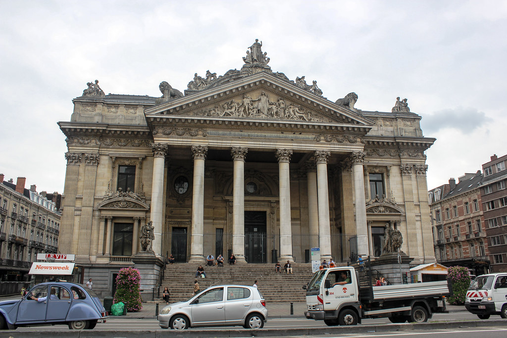 Fachada de la Bolsa de Bruselas con su arquitectura clásica y columnas imponentes, con vehículos y peatones en primer plano.