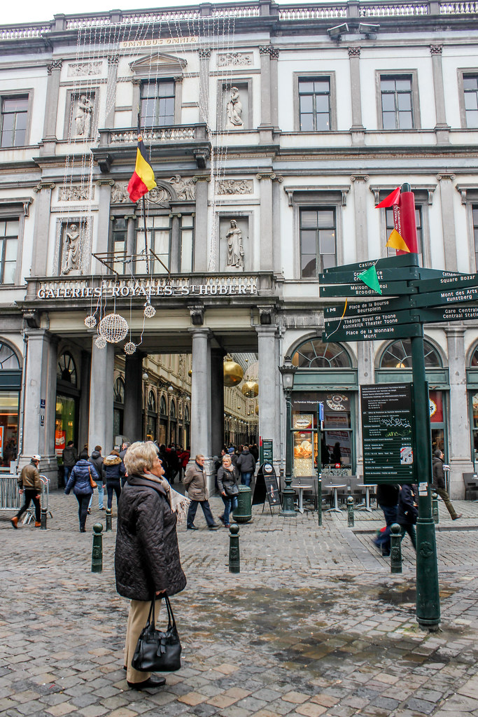 Visitantes caminando cerca de las Galerías Reales Saint-Hubert en Bruselas con banderas belgas.