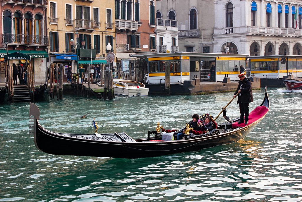 Gondolero navegando por un canal de Venecia con pasajeros.