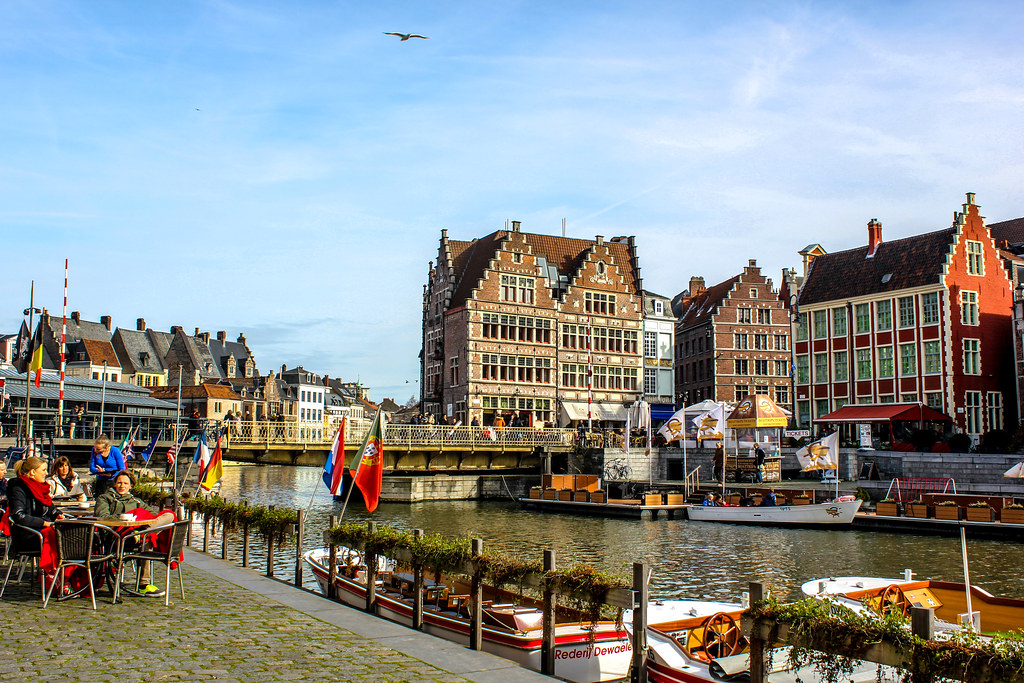 Vida urbana en la orilla del canal Graslei en Gante con casas tradicionales y barcos.