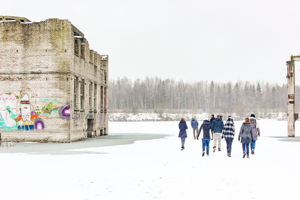 Grupo de personas caminando sobre un lago congelado junto a ruinas con grafiti en Rummu, Estonia.