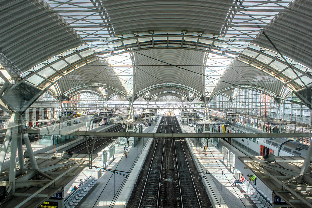 Vista interior de la estación de tren de Lovaina con techo de vidrio y estructura metálica.