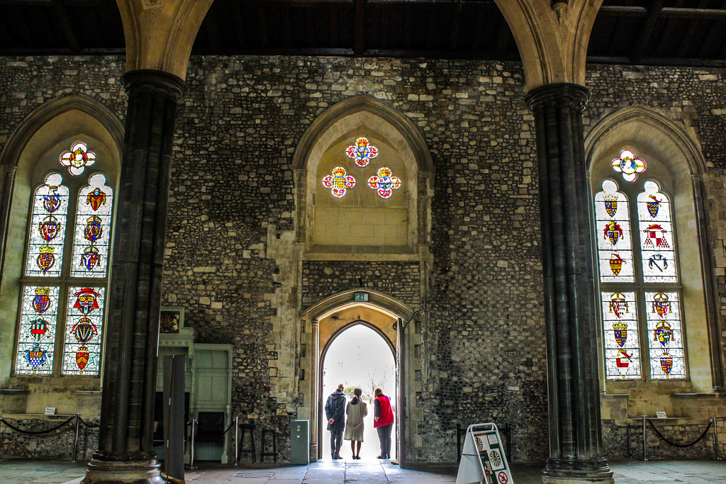 Interior del Gran Salón de Winchester con columnas y vitrales, personas caminando hacia la salida.