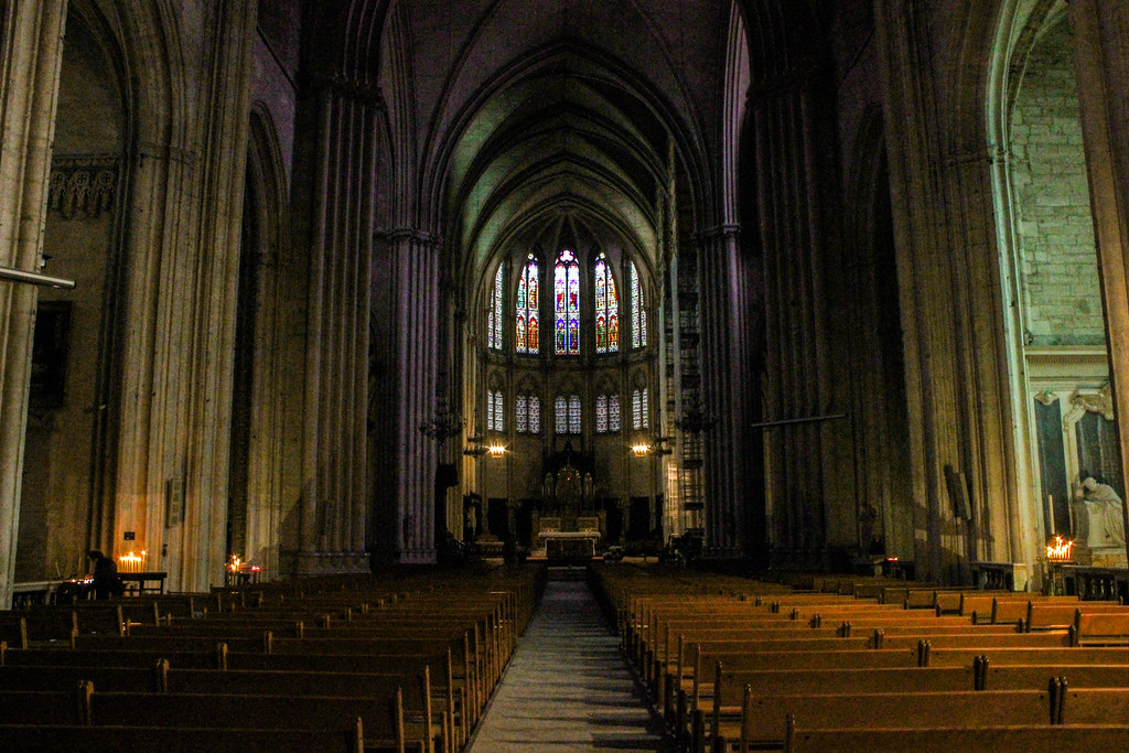 Interior sombrío de la catedral de Montpellier iluminado por la luz de un vitral colorido sobre el altar.