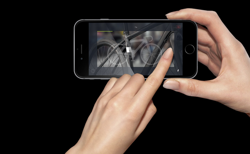 Manos utilizando la aplicación Bike-ID en un iPhone para registrar una bicicleta en un fondo oscuro.