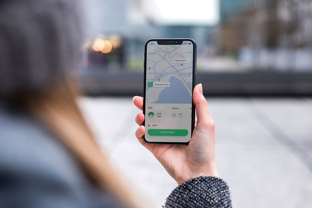 Persona sosteniendo un iPhone con la aplicación Bolt abierta mostrando opciones de viaje en un entorno urbano difuminado.