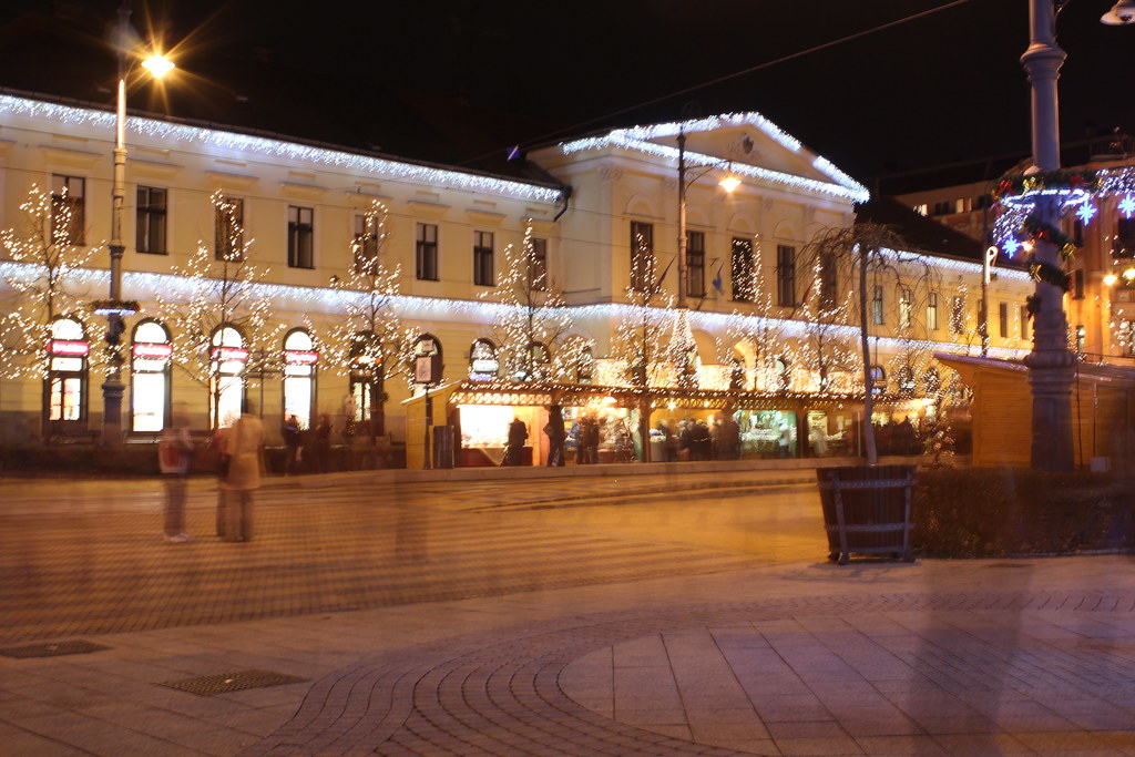 Mercado de Navidad iluminado en la noche en Debrecen con gente paseando.