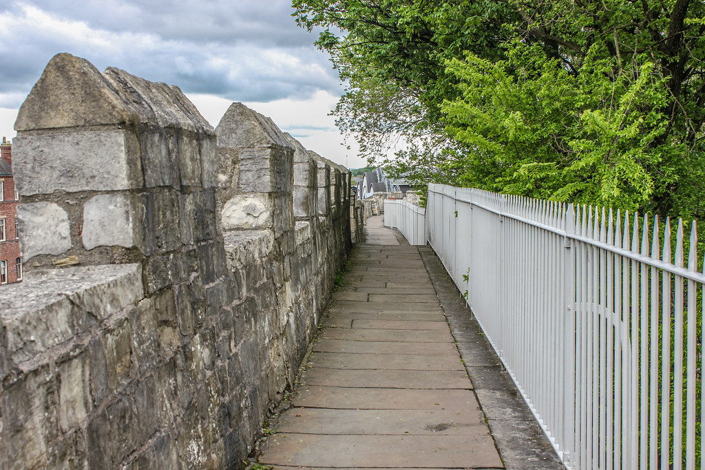 Camino peatonal sobre la antigua muralla de York con barandilla metálica y vegetación.