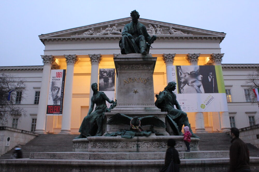 Fachada del Museo Nacional Húngaro en Budapest al atardecer con estatuas y visitantes.