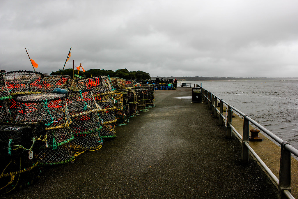 Nasas de pesca apiladas en Mudeford Quay con el mar al fondo en día lluvioso.