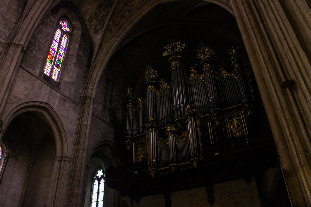 Órgano antiguo con detalles dorados en la sombría Catedral de Saint-Pierre de Montpellier junto a vitrales.