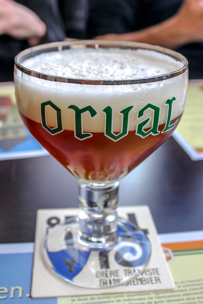 Primer plano de una copa de cerveza Orval verde sobre posavasos promocional.