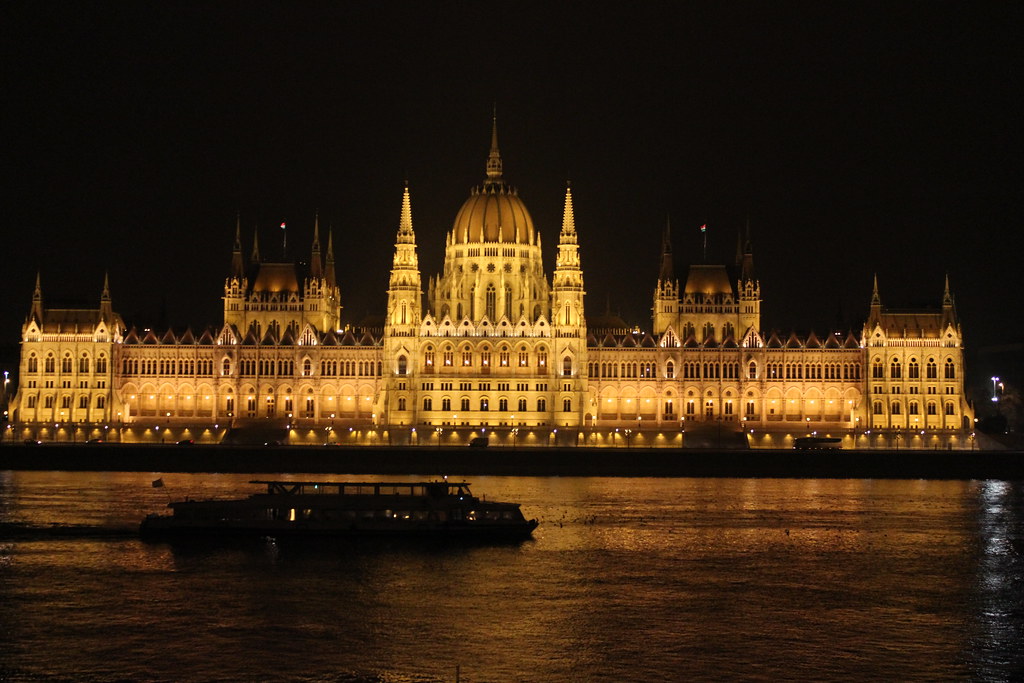 Vista nocturna del Parlamento de Budapest iluminado con un barco en el río Danubio.