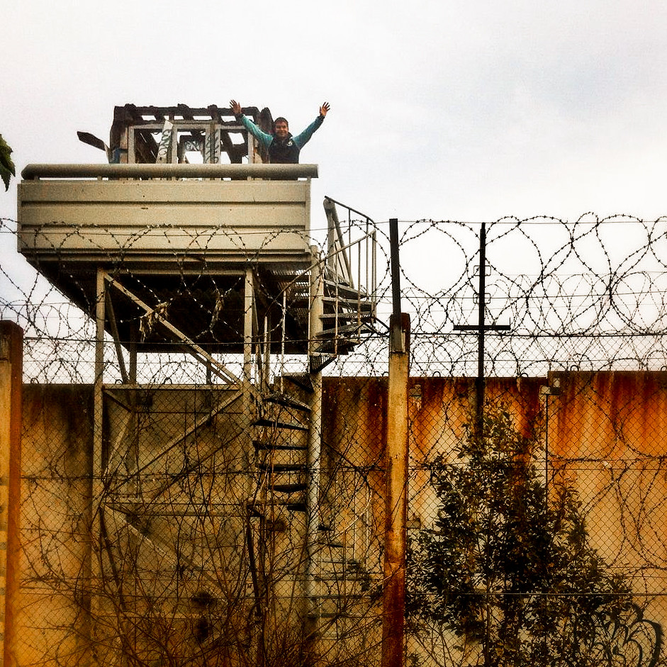 Coco saludando desde un puesto de vigía de la prisión de Rummu, detrás de una valla con alambre de púas.