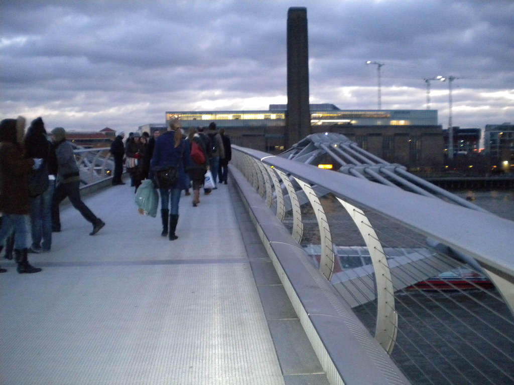 Personas cruzando el Millennium Bridge al atardecer en Londres.